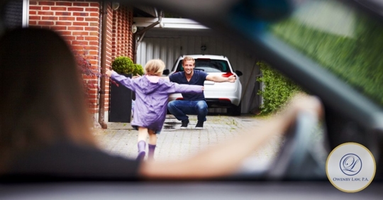 Child running to her father with open arms, while mother looks on from inside her car.